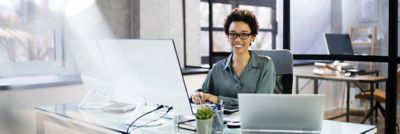 Woman sitting at desk, using big monitor with laptop on desk, Modern Device Management | DXC Technology